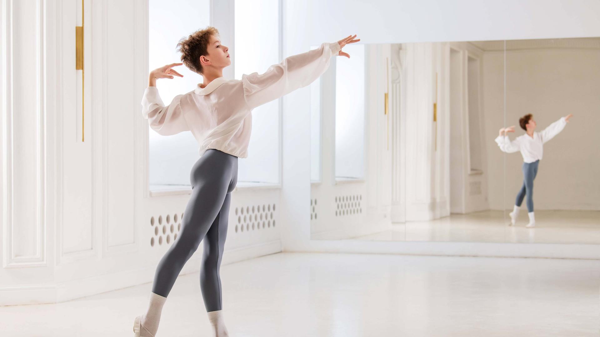 Ein Junge tanzt klassisches Ballett in einem hellen Saal mit Spiegel.