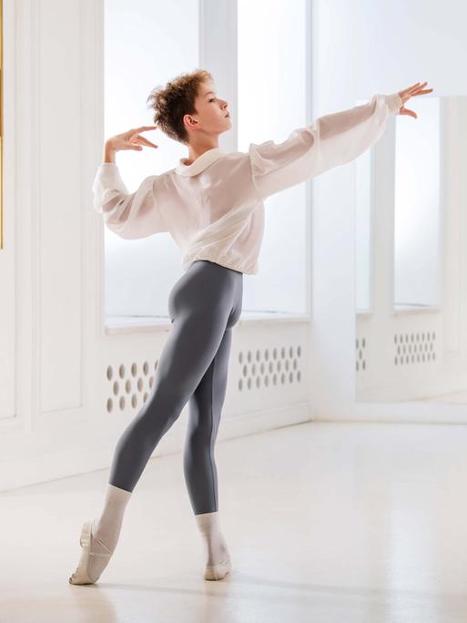 Ein Junge tanzt klassisches Ballett in einem hellen Saal mit Spiegel.