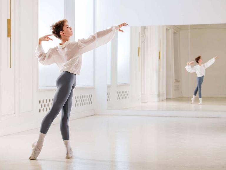 Ein Junge tanzt klassisches Ballett in einem hellen Saal mit Spiegel.