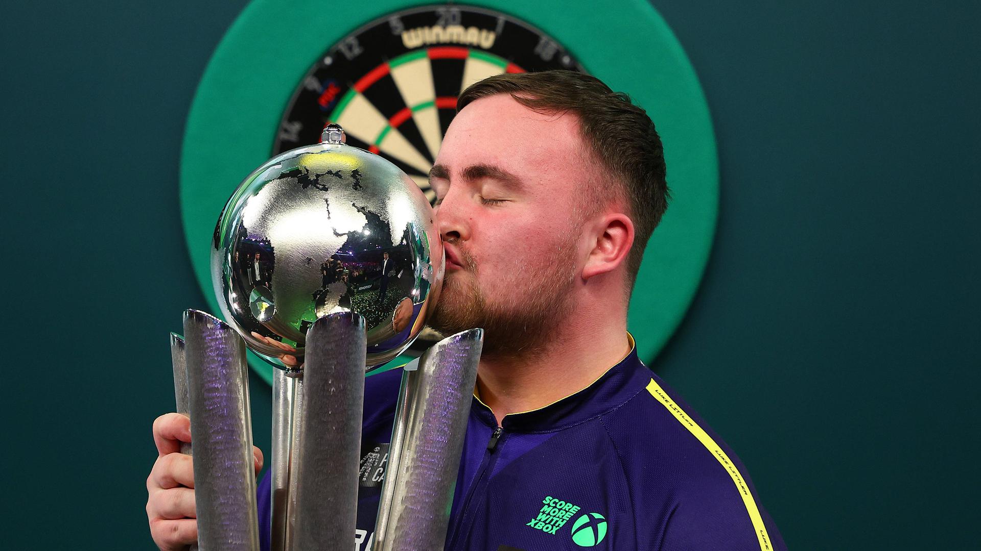 Darts-Profi Luke Littler küsst den WM-Pokal. 