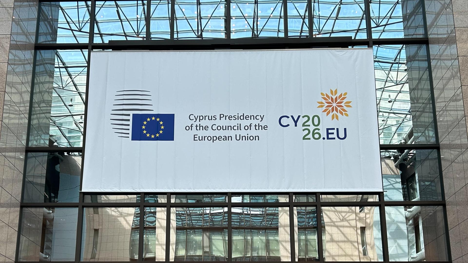An einer Fensterfront hängt ein Plakat mit der EU-Flagge und einem Hinweis auf die zyprische Ratspräsidentschaft.