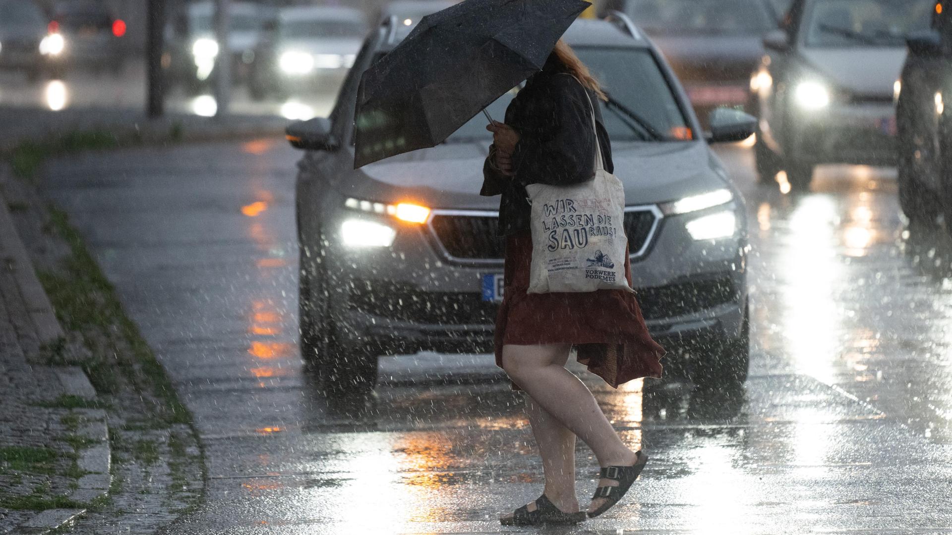 Eine Passantin überquert bei starkem Regen eine Straße mit einem Regenschirm.