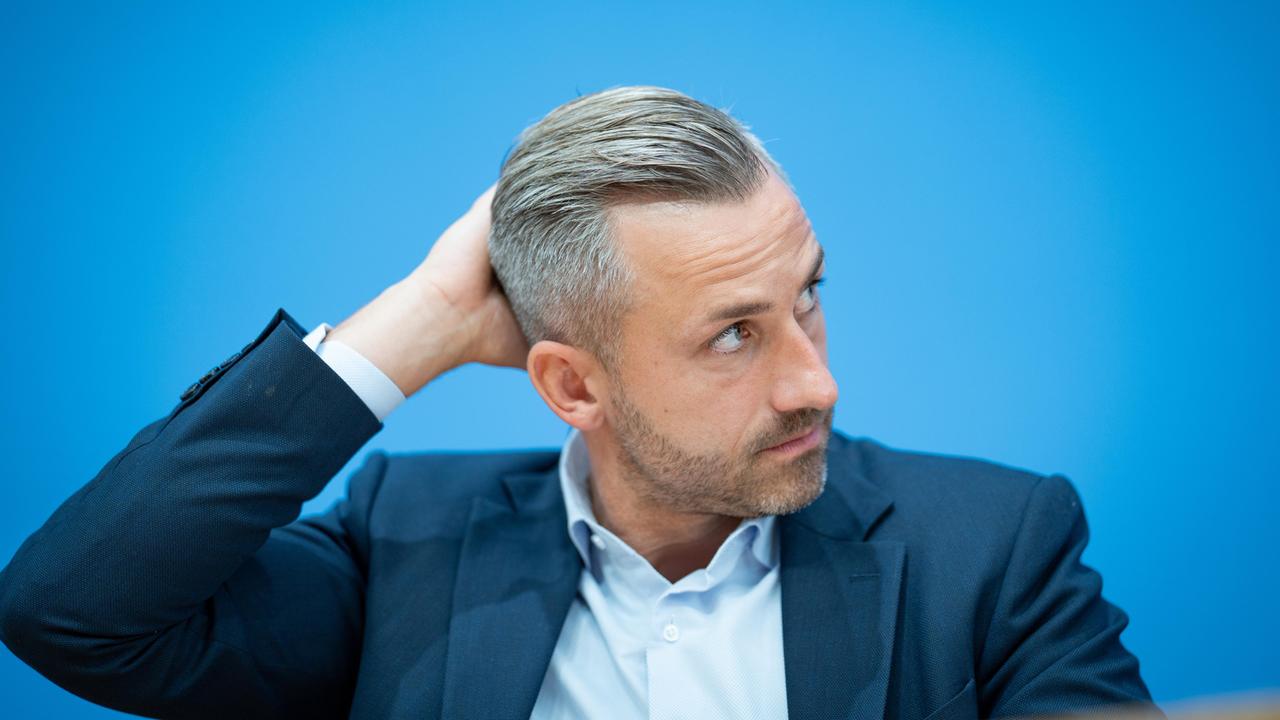 Ulrich Siegmund, im Sakko vor blauem Hintergrund, schaut zur Seite und greift sich an den Hinterkopf. Ulrich Siegmund, im Sakko vor blauem Hintergrund, schaut zur Seite und greift sich an den Hinterkopf.