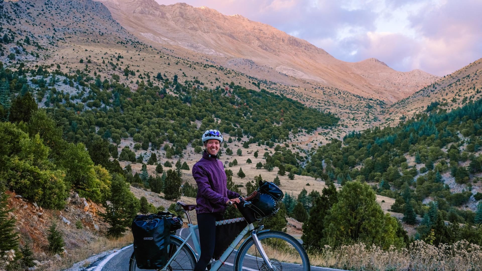 Liz Steinwandel auf Ihrem Fahrrad auf dem Weg nach Baku. Zu sehen auf einer Landstraße. Dahinter ein hoher Gipfel. 