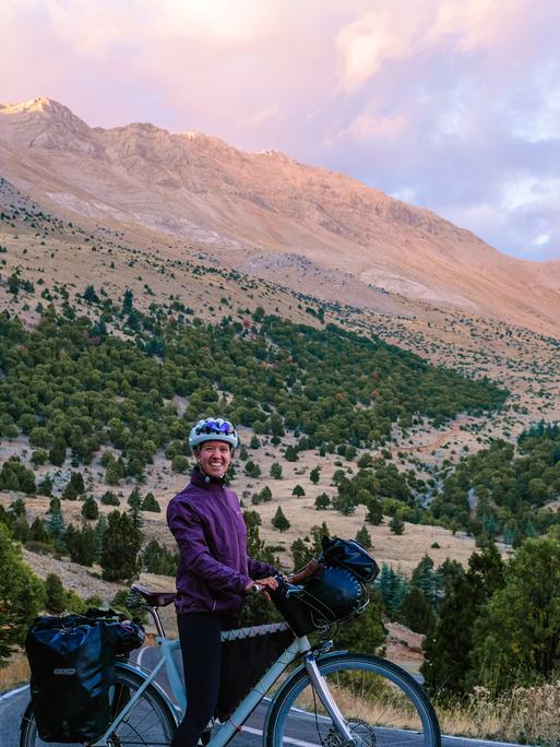 Liz Steinwandel auf Ihrem Fahrrad auf dem Weg nach Baku. Zu sehen auf einer Landstraße. Dahinter ein hoher Gipfel. 