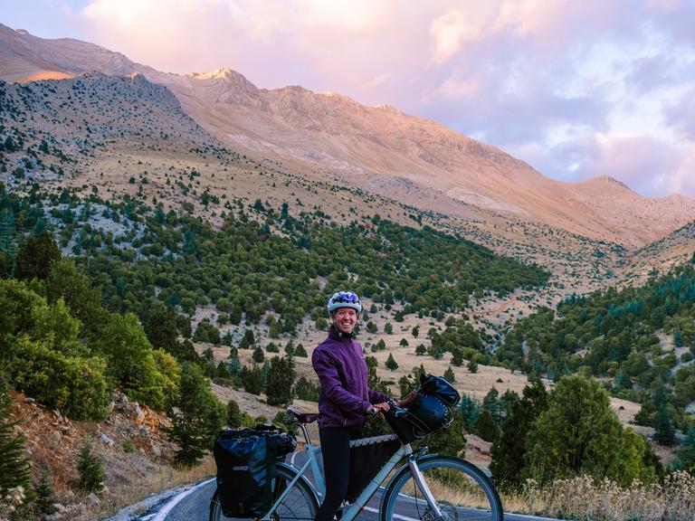 Liz Steinwandel auf Ihrem Fahrrad auf dem Weg nach Baku. Zu sehen auf einer Landstraße. Dahinter ein hoher Gipfel. 