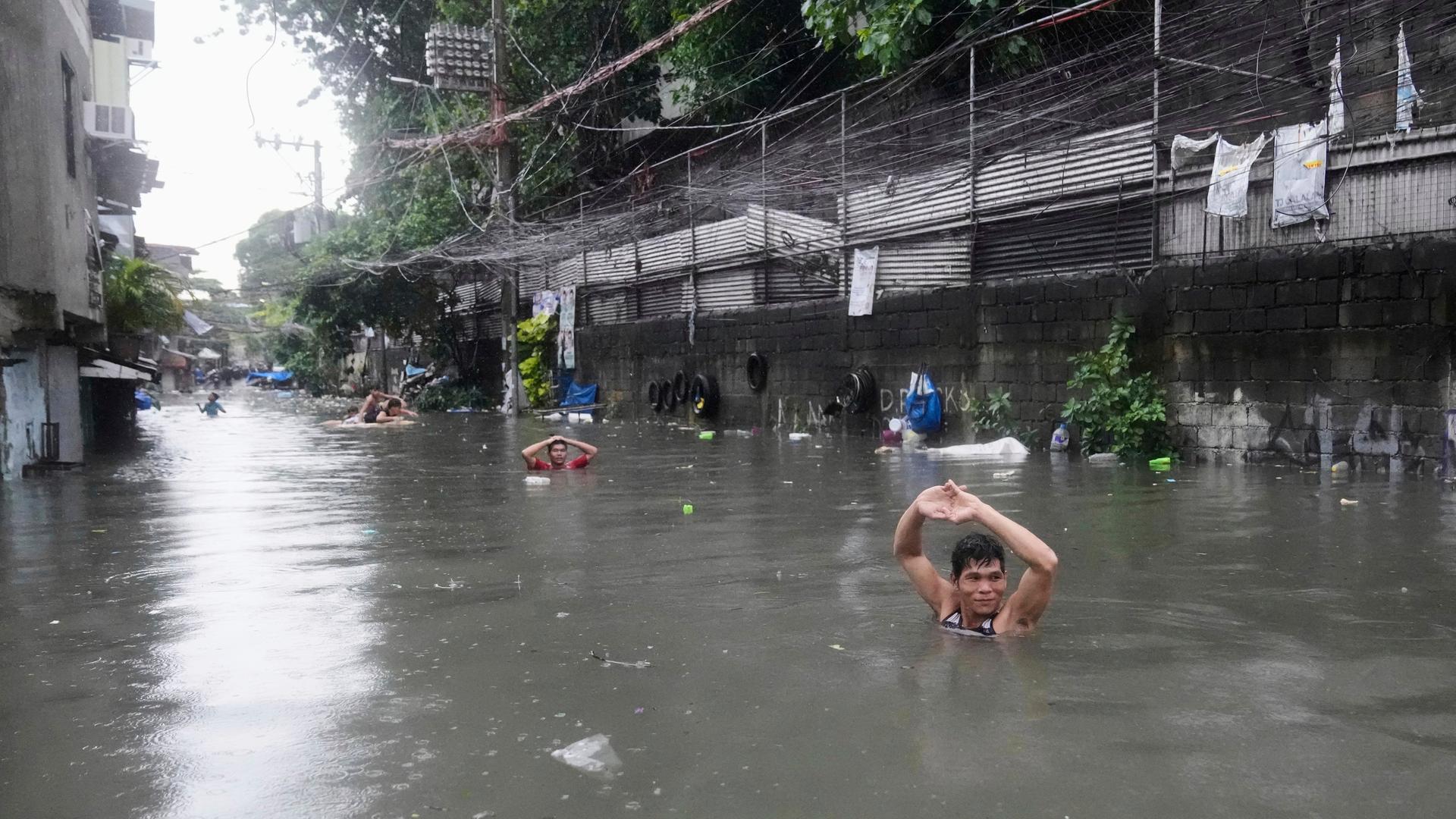 Menschen versuchen, auf einer überfluteten Straße voranzukommen. Sie stehen schulterhoch im Wasser.
Menschen versuchen, auf einer überfluteten Straße voranzukommen. Sie stehen schulterhoch im Wasser.