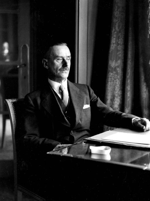 Historisches Schwarzweißfoto von Thomas Mann, der an einem Schreibtisch sitzt.