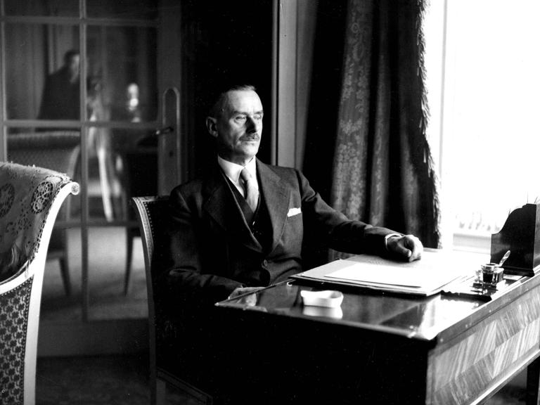 Historisches Schwarzweißfoto von Thomas Mann, der an einem Schreibtisch sitzt.