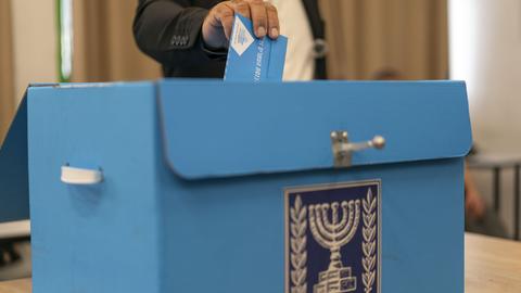 Ein Mann steckt seinen Wahlumschlag in eine Wahlkiste, auf der der siebenarmige Leuchter zu sehen ist.