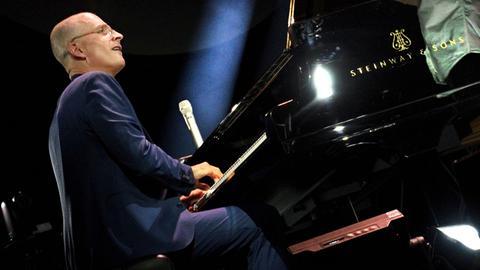 Ein Mann im blauen Anzug spielt Klavier. 