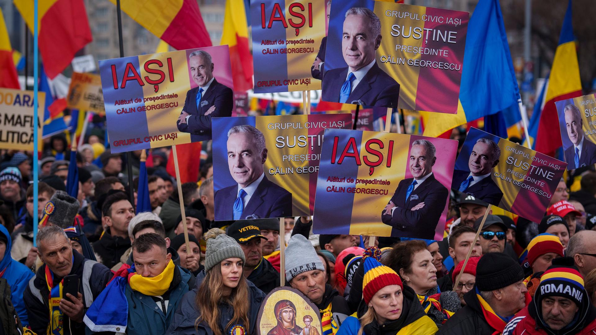 Menschen halten Bilder von C.Georgescu während einer Demonstration vor dem Regierungssitz.