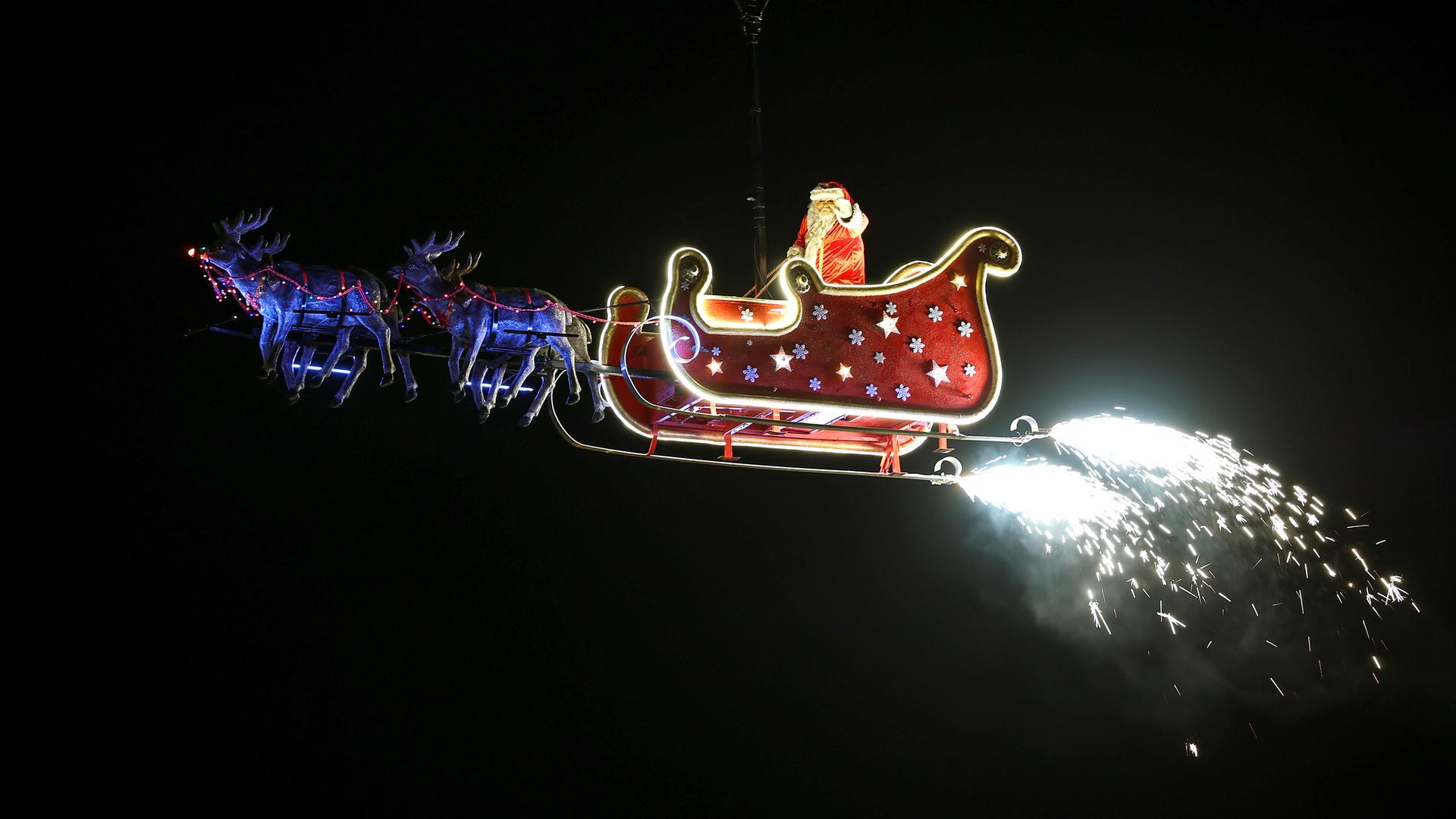 Ein Weihnachtsmann schwebt in seinem Schlitten gezogen von Rentieren durch den Himmel. 