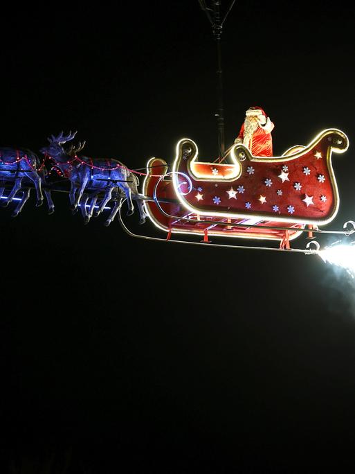 Ein Weihnachtsmann schwebt in seinem Schlitten gezogen von Rentieren durch den Himmel. 