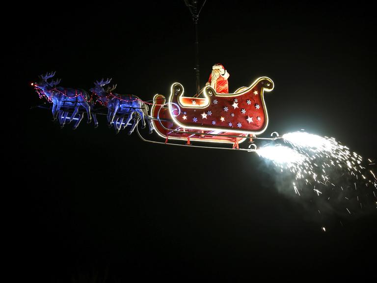 Ein Weihnachtsmann schwebt in seinem Schlitten gezogen von Rentieren durch den Himmel. 