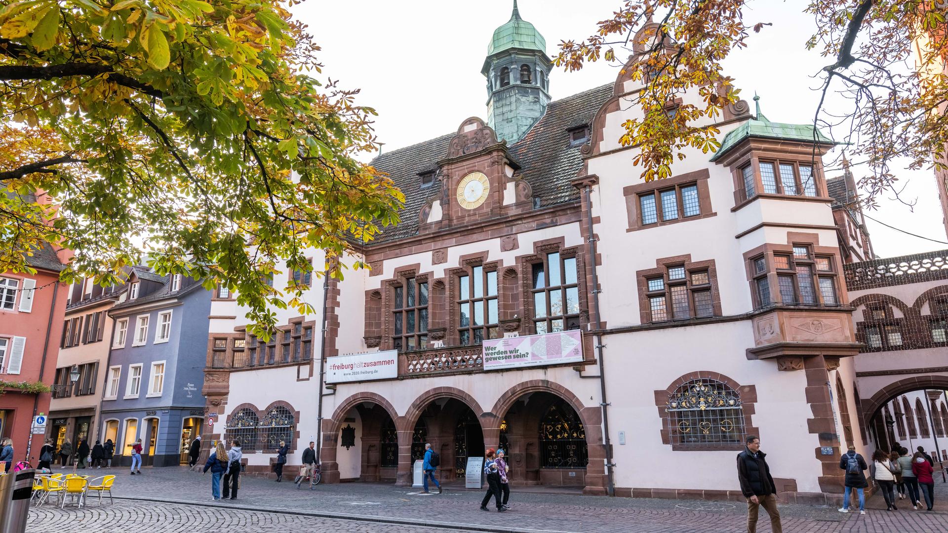 Herbstlich gefärbtes Laub hängt an den Bäumen auf dem Rathausplatz, im Hintergrund ist das Freiburger Rathaus zu sehen. Herbstlich gefärbtes Laub hängt an den Bäumen auf dem Rathausplatz, im Hintergrund ist das Freiburger Rathaus zu sehen.