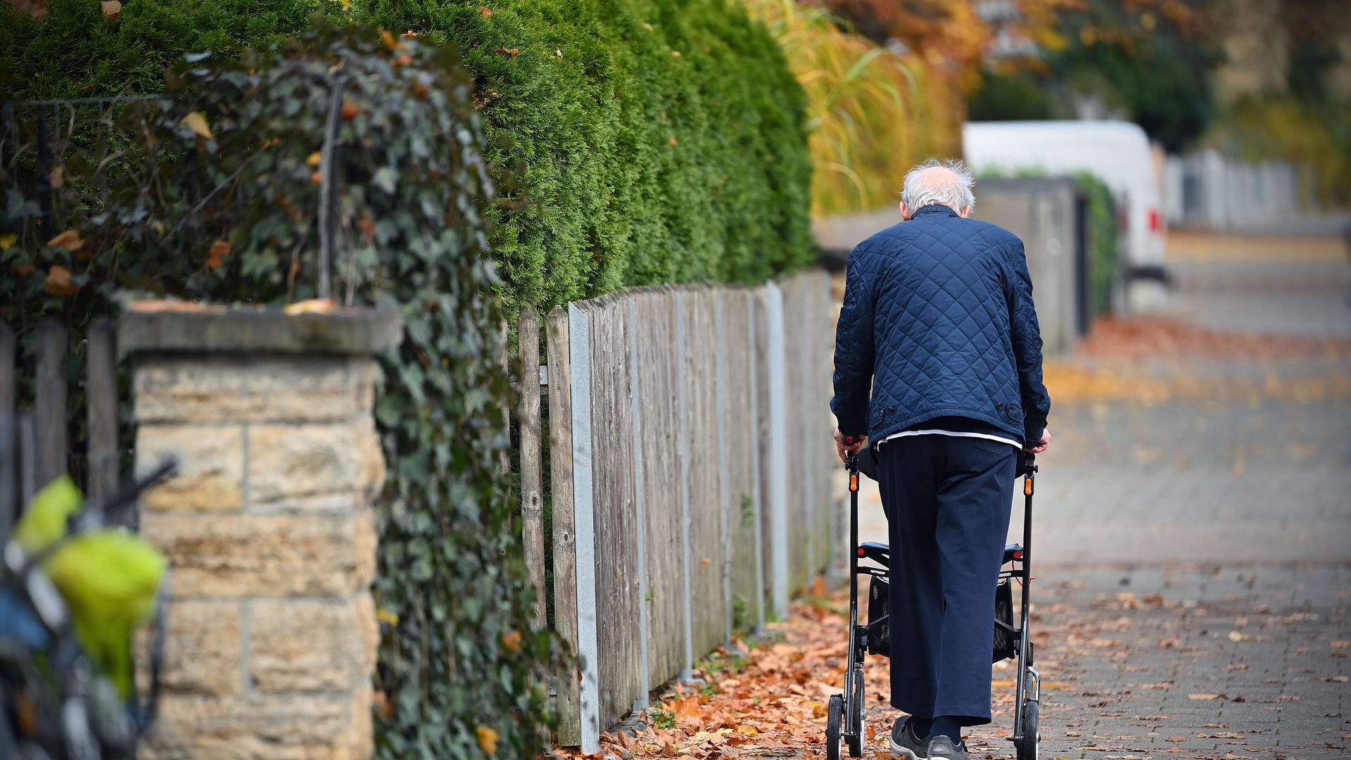 Ein Rentner schiebt seinen Rollator einen Gehweg entlang.