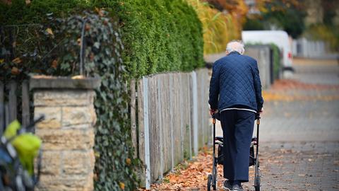 Ein Rentner schiebt seinen Rollator einen Gehweg entlangt.