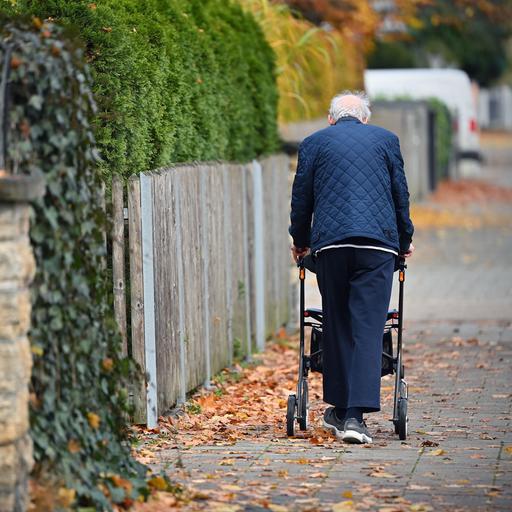 Ein Rentner schiebt seinen Rollator einen Gehweg entlangt.