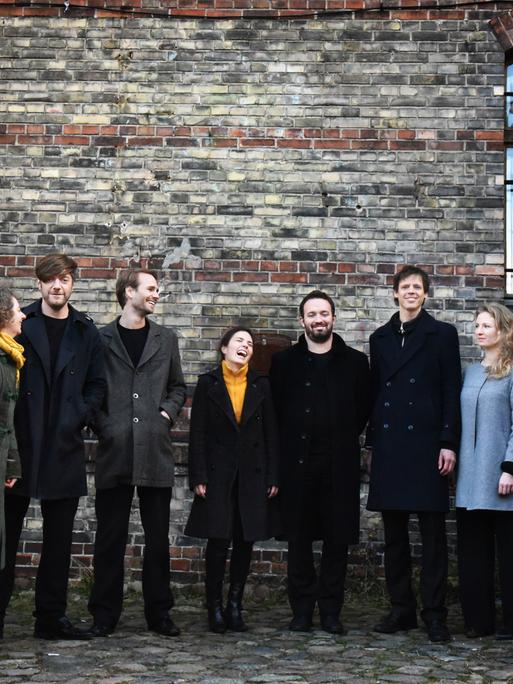 Die 10 Ensemblemitglieder stehen vor der Mauer eines alten Hauses