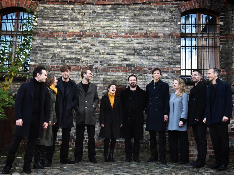 Die 10 Ensemblemitglieder stehen vor der Mauer eines alten Hauses