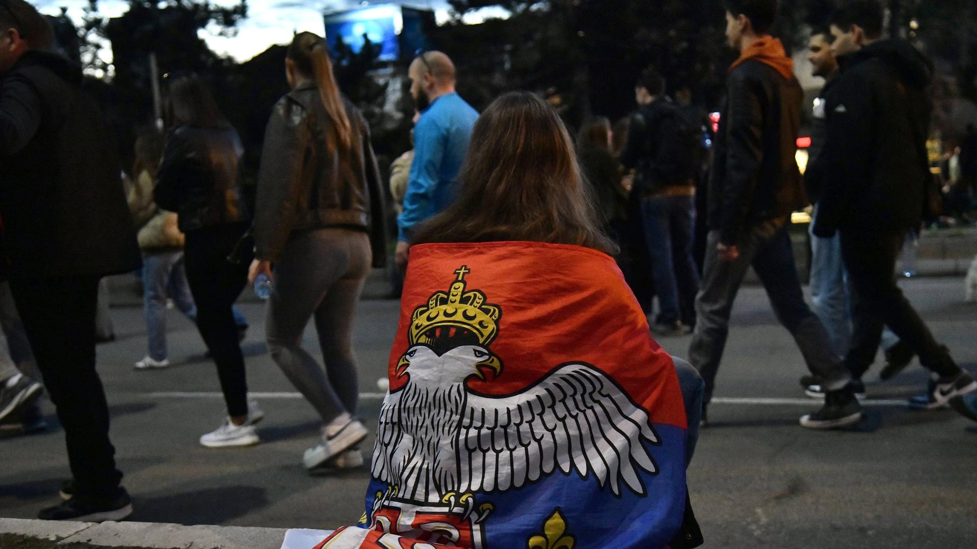 Eine protestierende Studentin hat eine serbische Flagge umgehängt, sie sitzt auf dem Boden.