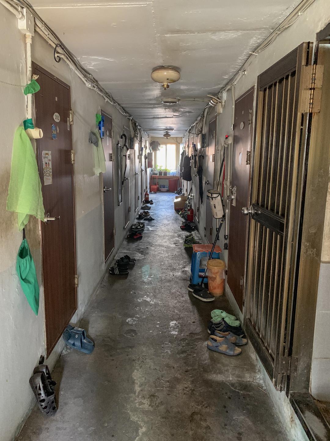 Ein enger Hausflur mit feuchten Wänden ist zu sehen, vor dessen Wohnungstüren Schuhe stehen.