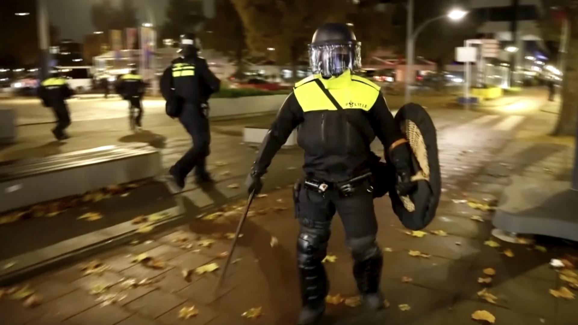 In Amsterdam gab es erneut Krawalle. Polizisten laufen am Abend durch eine Straße. 