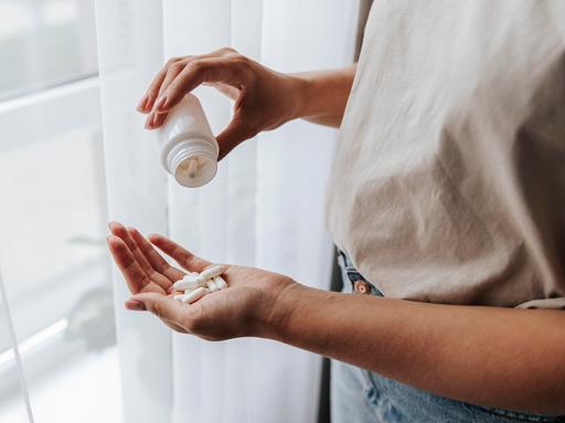 Eine Frau steht am Fenster und schüttet weiße Pillen aus einer weißen Dose in ihre Hand.