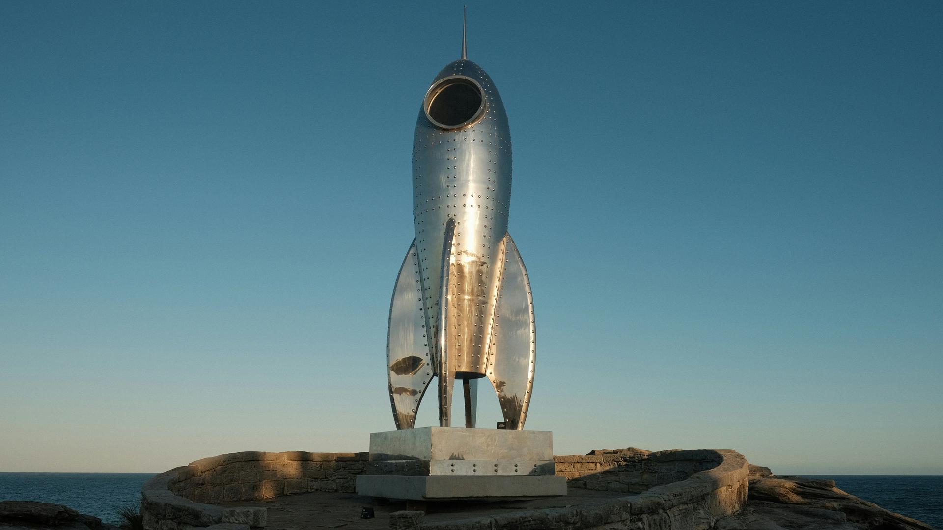 Blick auf eine Art Denkmal, das wie eine kindliche Rakete aus Metall aussieht.