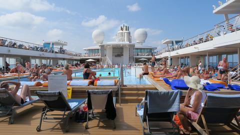 Passagiere des Kreuzfahrtschiffs Mein Schiff 3 genießen den Tag am Pool. 