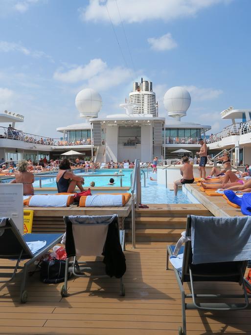 Passagiere des Kreuzfahrtschiffs Mein Schiff 3 genießen den Tag am Pool. 