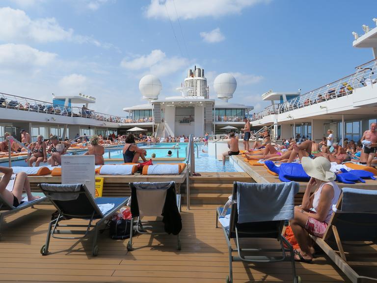 Passagiere des Kreuzfahrtschiffs Mein Schiff 3 genießen den Tag am Pool. 