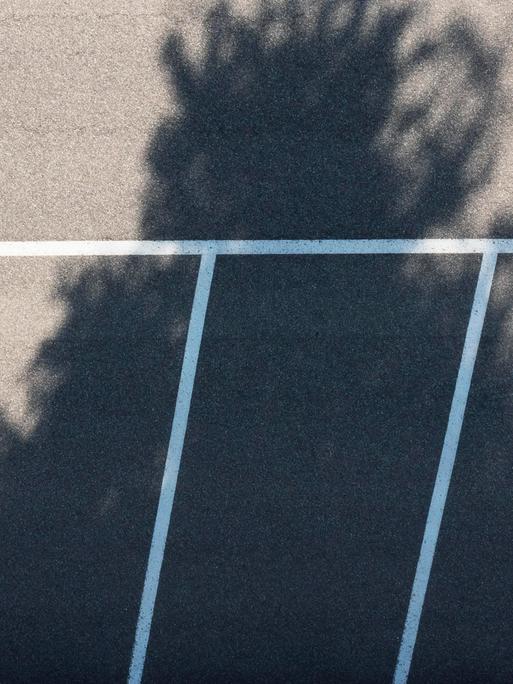 Drohnenaufnahme von einem leeren Parkplatz, auf den der Schatten eines Baumes fällt