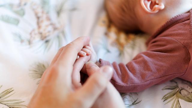 Eine Mutter und ein Vater legen ihre Hände auf die Hand von ihrem wenige Wochen alten Baby.