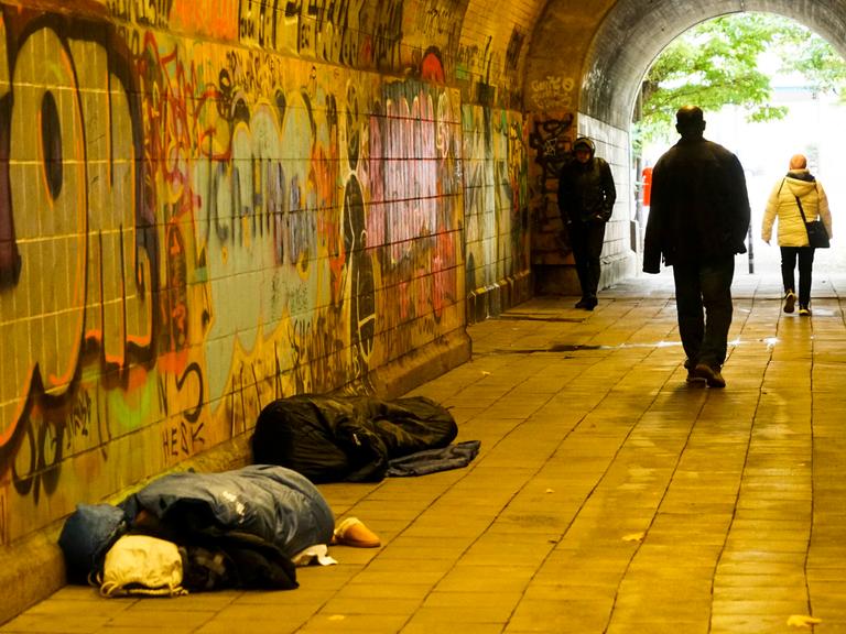 Oblachlose Menschen schlafen am helllichten Tag auf dem Boden mit ihren Habseligkeiten. Passanten gehen an den Menschen auf dem Boden vorbei. Es ist in einem Fußgängertunnel in Hamburg. Oblachlose Menschen schlafen am helllichten Tag auf dem Boden mit ihren Habseligkeiten. Passanten gehen an den Menschen auf dem Boden vorbei. Es ist in einem Fußgängertunnel in Hamburg.