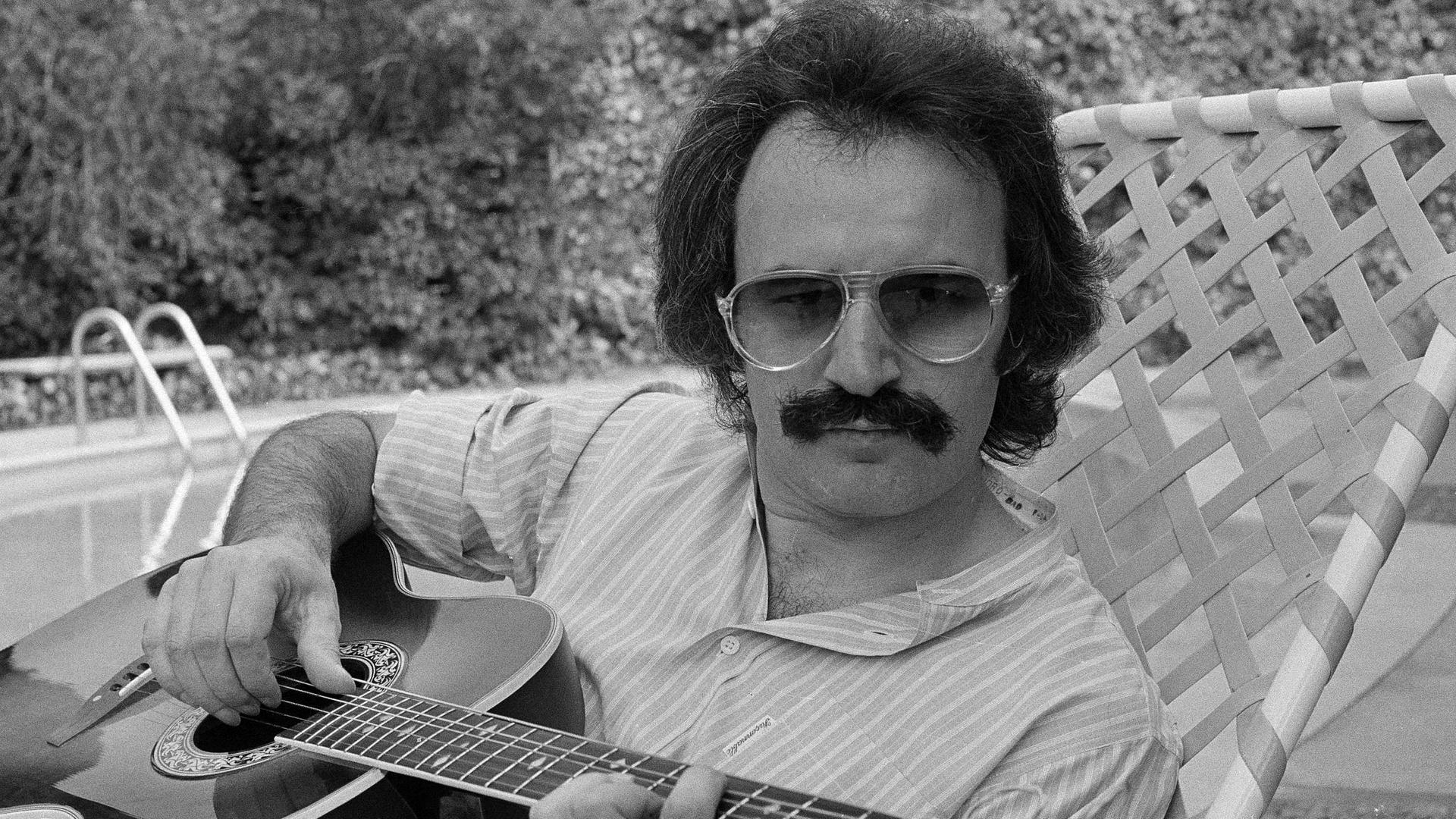 Ein Mann mit Schnurrbart und Sonnenbrille spielt Gitarre.