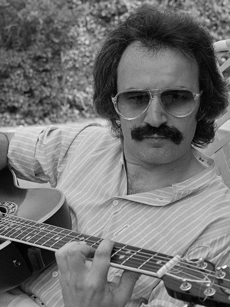 Ein Mann mit Schnurrbart und Sonnenbrille spielt Gitarre.