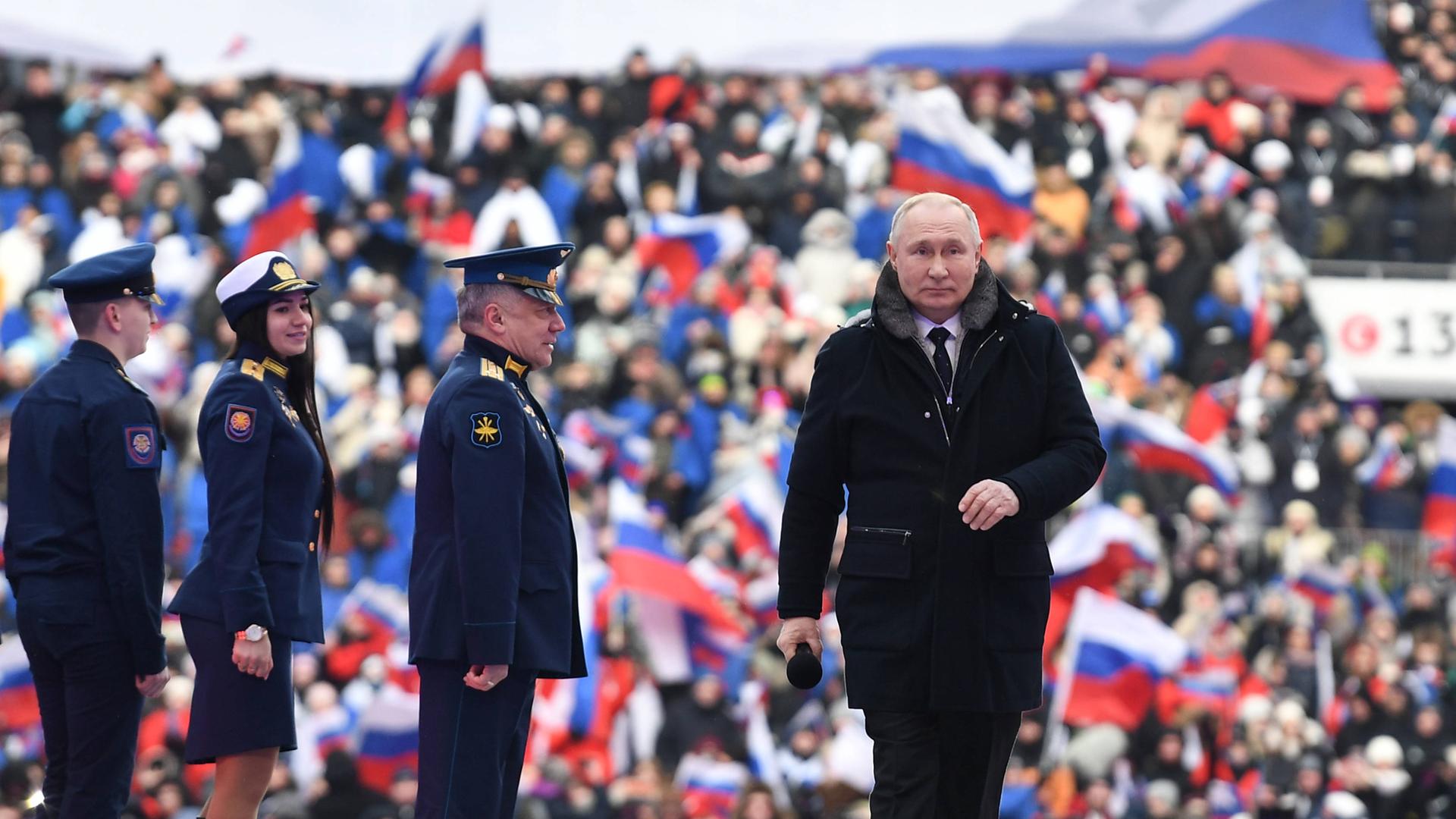 Präsident Putin geht an russischen Soldaten auf einer Bühne vorbei. Im Hintergrund schwenken die Zuschauer russische Fahnen.