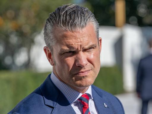 Nahaufnahme des US-Verteidigungsministers Pete Hegseth in blauem Anzug und roter Krawatte. Er kneift seine von der Sonne geblendeten Augen zusammen. Nahaufnahme des US-Verteidigungsministers Pete Hegseth in blauem Anzug und roter Krawatte. Er kneift seine von der Sonne geblendeten Augen zusammen.