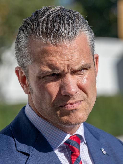 Nahaufnahme des US-Verteidigungsministers Pete Hegseth in blauem Anzug und roter Krawatte. Er kneift seine von der Sonne geblendeten Augen zusammen. Nahaufnahme des US-Verteidigungsministers Pete Hegseth in blauem Anzug und roter Krawatte. Er kneift seine von der Sonne geblendeten Augen zusammen.