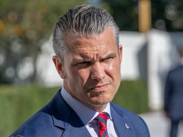 Nahaufnahme des US-Verteidigungsministers Pete Hegseth in blauem Anzug und roter Krawatte. Er kneift seine von der Sonne geblendeten Augen zusammen. Nahaufnahme des US-Verteidigungsministers Pete Hegseth in blauem Anzug und roter Krawatte. Er kneift seine von der Sonne geblendeten Augen zusammen.