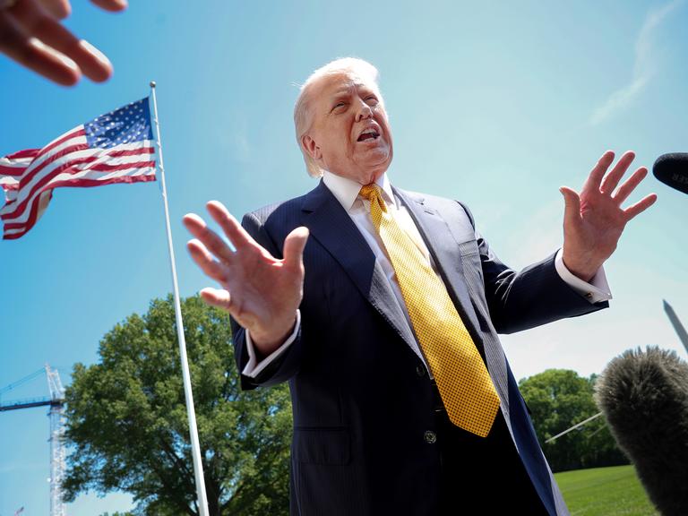 US-Präsident Donald Trump spricht mit Journalisten. Das Foto ist von schräg unten aufgenommen. Im Hintergrund ist eine US-Flagge und blauer Himmel zu sehen. US-Präsident Donald Trump spricht mit Journalisten. Das Foto ist von schräg unten aufgenommen. Im Hintergrund ist eine US-Flagge und blauer Himmel zu sehen.