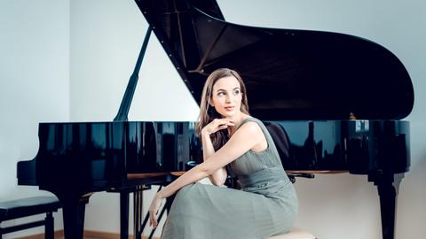 Die junge Pianistin Mitra Kotte sitzt vor einem aufgeklappten Flügel und schaut über ihre Schulter in die Ferne.