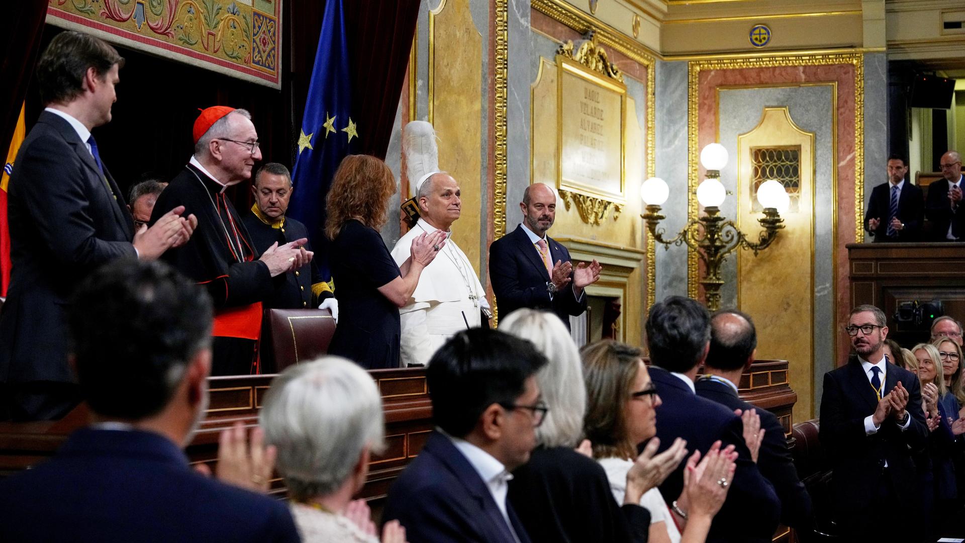 Politiker und Geistliche applaudieren in Richtung von Papst Leo, der am Rednerpult des reich verzierten spanischen Plenarsaals steht. Politiker und Geistliche applaudieren in Richtung von Papst Leo, der am Rednerpult des reich verzierten spanischen Plenarsaals steht.