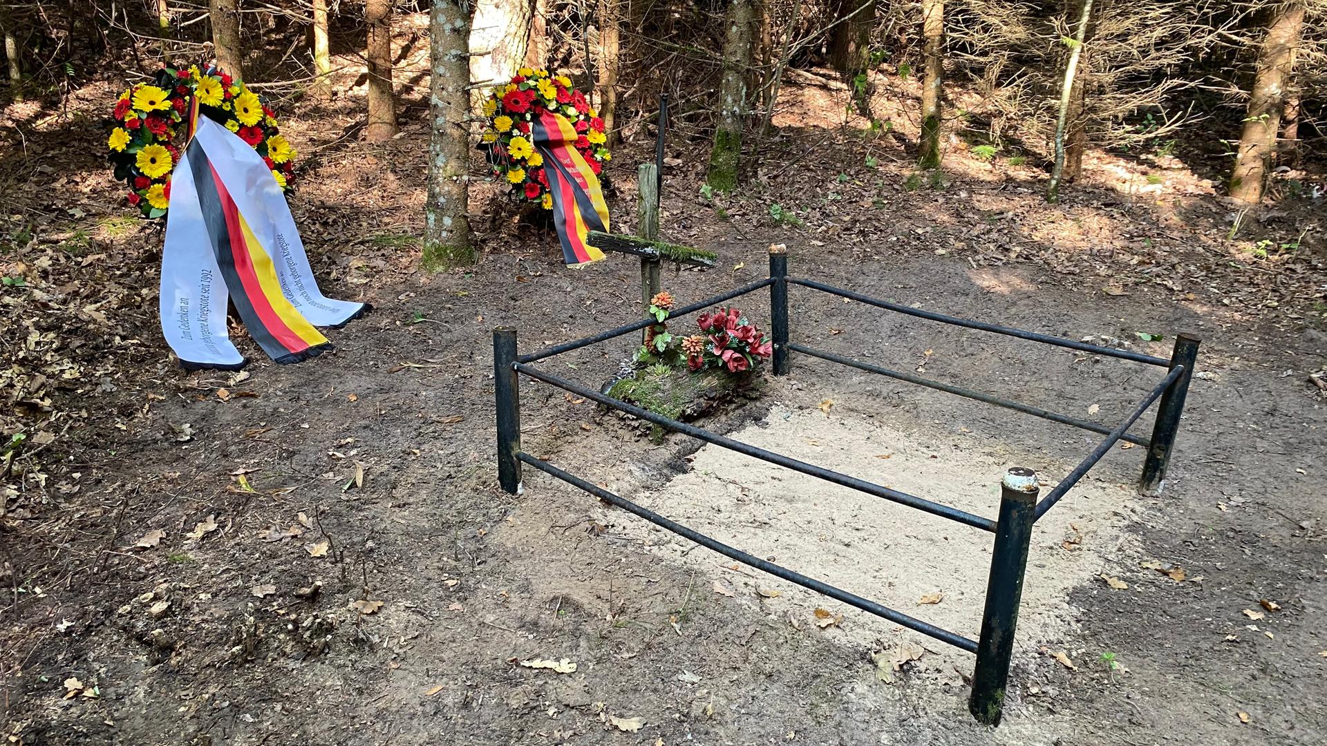 Eine mit Eisengitter umzäunte Grabstelle, im Hintergrund Kränze mit der deutschen und der litauischen Flagge.