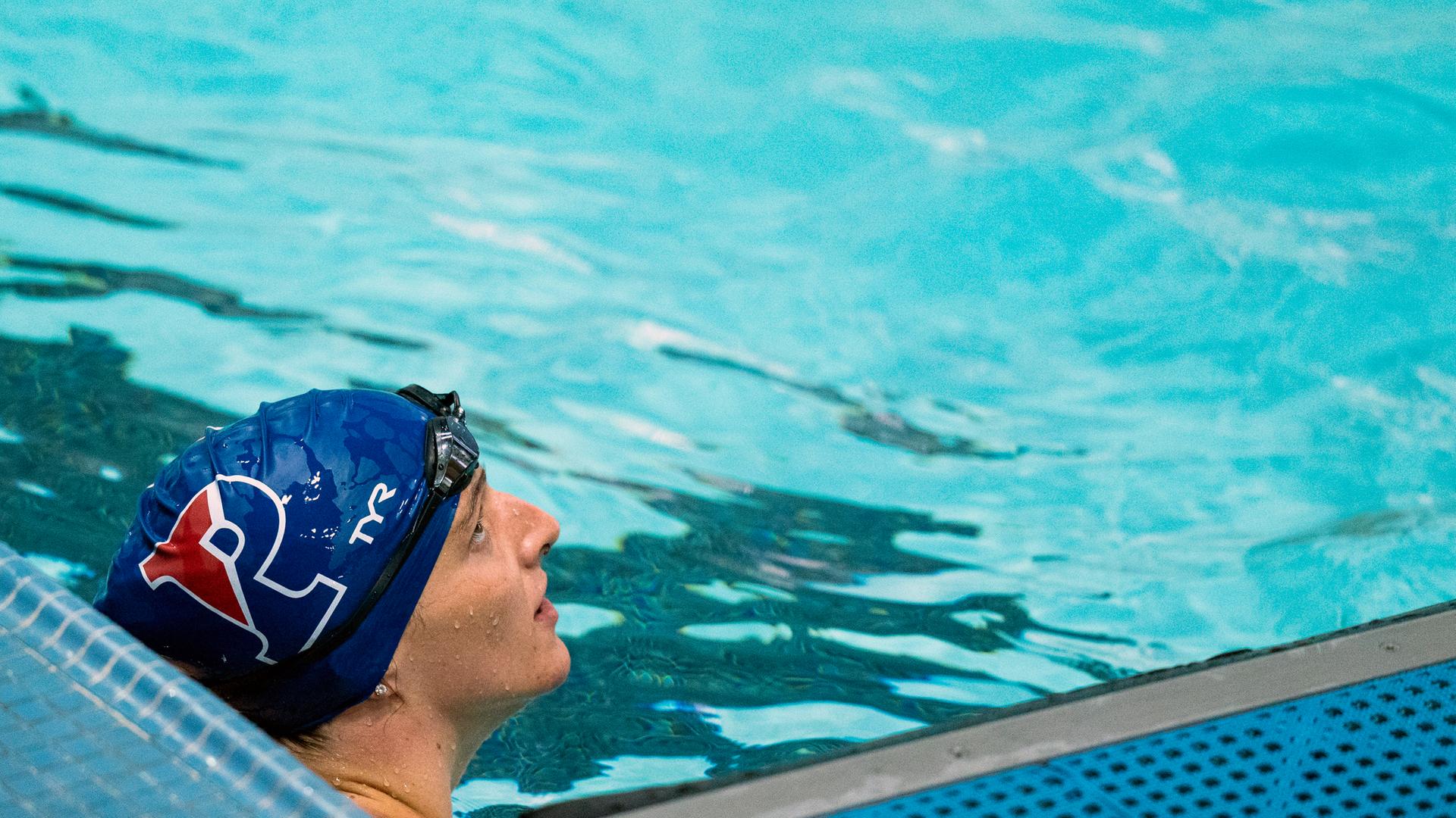 Die Schwimmerin Lia Thomas mit einer Badekappe bekleidet im Becken. Ihr Blick ist nach oben gerichtet. 