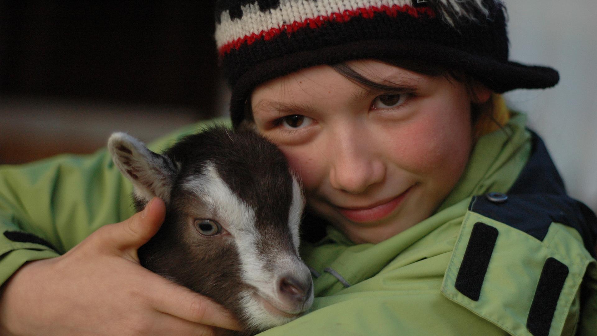 Ein Mädchen hält eine kleine Ziege im Arm.