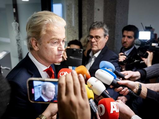 Geert Wilders steht vor vielen Reporterinnen und Reportern, die Mikrofone in seine Richtung strecken.