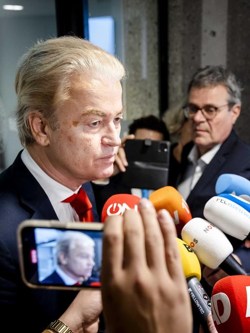 Geert Wilders steht vor vielen Reporterinnen und Reportern, die Mikrofone in seine Richtung strecken.